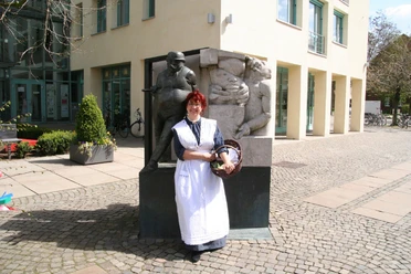 Anna - Frau vom Zigarrenmacher Eine Frau im historischen Kleid steht vor einer Skulptur eines Zigarrenmachers und einer Frau.