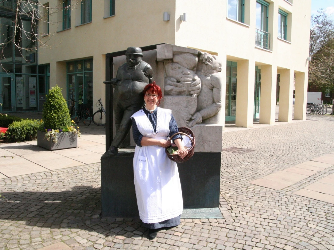 Anna - Frau vom Zigarrenmacher Eine Frau im historischen Kleid steht vor einer Skulptur eines Zigarrenmachers und einer Frau.