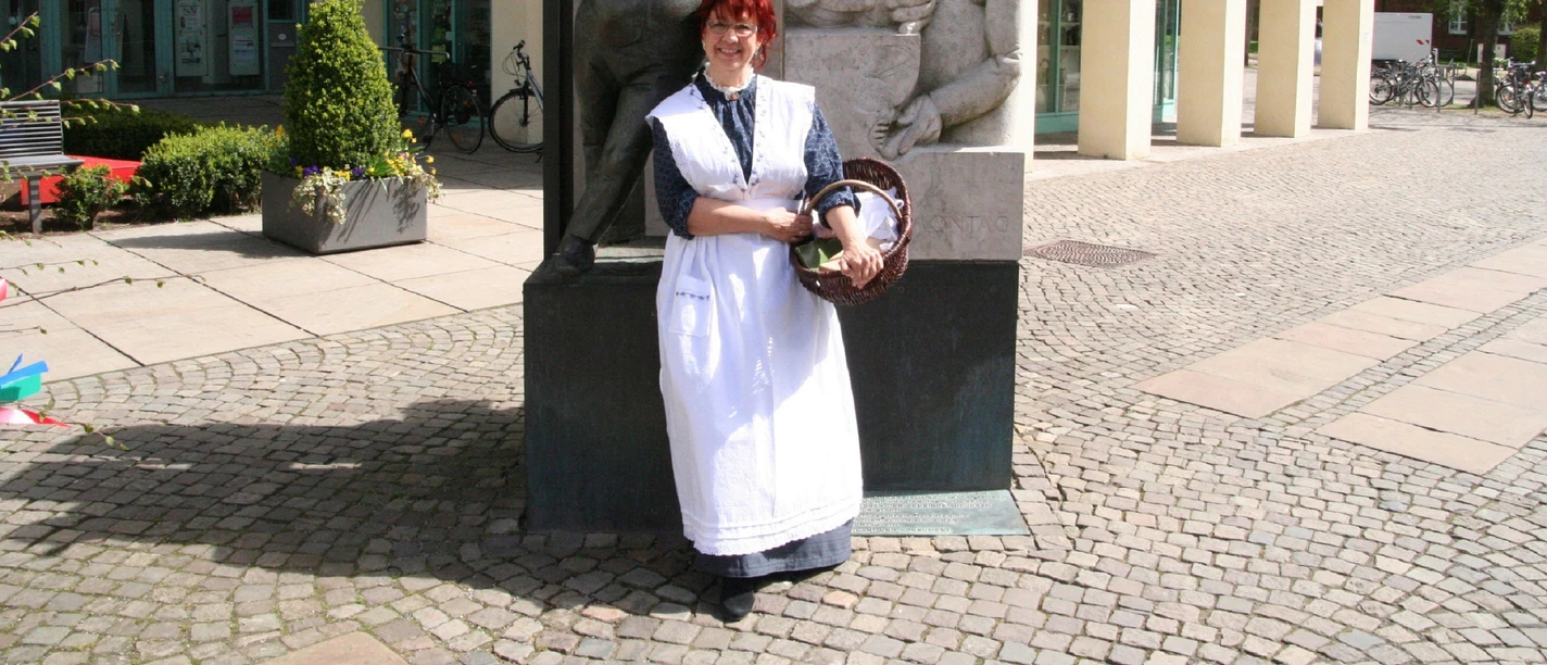 Anna - Frau vom Zigarrenmacher Eine Frau im historischen Kleid steht vor einer Skulptur eines Zigarrenmachers und einer Frau.