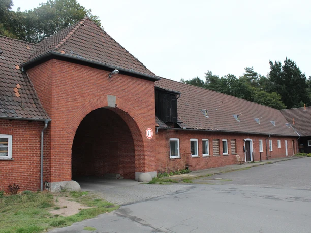 Waldsiedlung Liebenau Eingangsbereich eines historischen, roten Backsteingebäudes mit großem Torbogen in einer Waldumgebung.