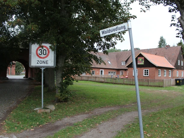 Eingebettet in grüner Umgebung zeigt ein 30er-Zone Schild den Weg entlang traditioneller Gebäude.