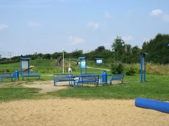 In einem öffentlichen Park stehen blaue Bänke um einen Tisch, umgeben von grüner Landschaft.