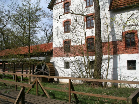 Historische Wassermühle mit rotem Ziegeldach, umgeben von grüner Natur, mit einem hölzernen Mühlrad.