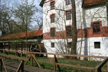 Wassermühle Blenhorst Historische Wassermühle mit rotem Ziegeldach, umgeben von grüner Natur, mit einem hölzernen Mühlrad.