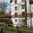 Wassermühle Blenhorst Historische Wassermühle mit rotem Ziegeldach, umgeben von grüner Natur, mit einem hölzernen Mühlrad.