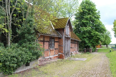 Historische Wassermühle Heuermann aus rotem Backstein, umgeben von Bäumen, mit leicht bemoostem Dach.