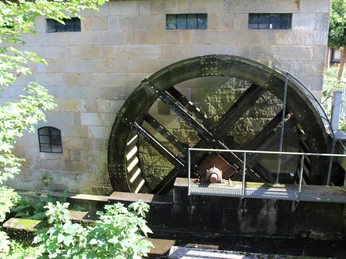 Wassermühle Sudweyhe Wasserrad einer historischen Mühle in Sudweyhe zwischen Bäumen und Steinmauer, stillstehend und sonnenbeschienen.