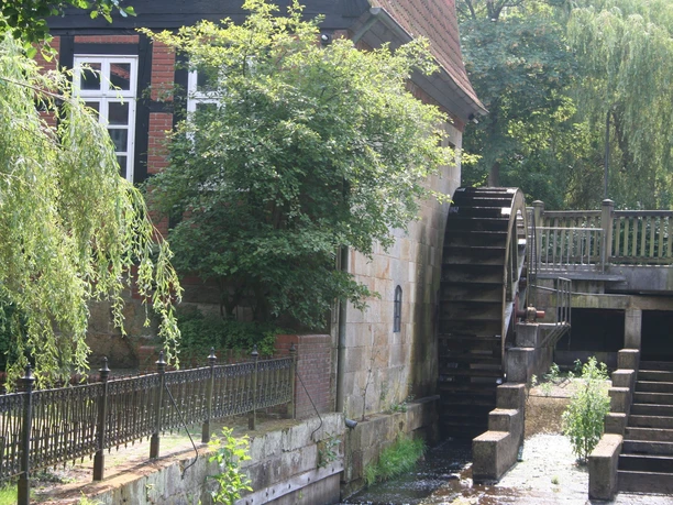 Wassermühle Sudweyhe Wassermühle mit drehendem Wasserrad; im Hintergrund umgeben von Bäumen und Fachwerkarchitektur.