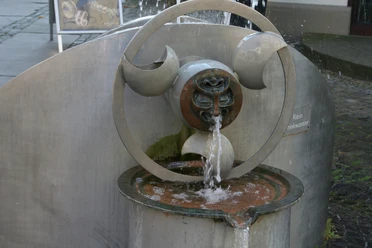 Moderner Wasserspielbrunnen aus Metall, künstlerisch gestaltet, sprudelndes Wasser und Details.