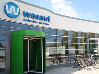 Wesavi Eingang Moderner Eingang des Wesavi-Badezentrums mit grünem Glasdrehtor und geparkten Fahrrädern davor.Modern entrance to the Wesavi bathing center with green glass revolving gate and parked bicycles in front of it.Moderne indgang til Wesavi badecenter med grøn glasdrejeport og parkerede cykler foran.Moderne ingang van het Wesavi zwemcentrum met groen glazen draaihek en geparkeerde fietsen ervoor.