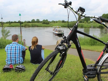 Menschen genießen den Anblick einer vorbeifahrenden Weserfähre bei Ahsen-Oetzen, Fahrräder im Vordergrund.