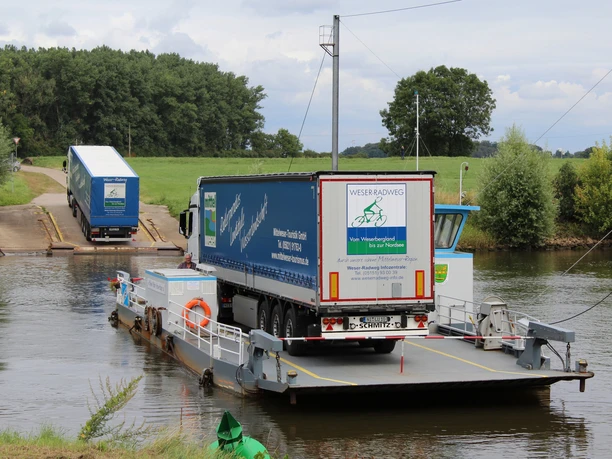 LKW auf der Fähre Schweringen Ein LKW befindet sich auf einer kleinen Fähre, die eine ruhige Flussüberquerung in ländlicher Umgebung vollzieht.