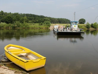 Radfahrer nutzen die Weserfähre in Schweringen, während im Vordergrund ein gelbes Boot im Wasser liegt.