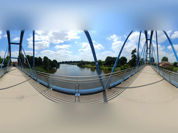 Fußgängerbrücke Panorama - Wesertorbrücke Blick von der Wesertorbrücke in Minden auf die Weser, flankiert von grünen Bäumen und blauem Himmel.