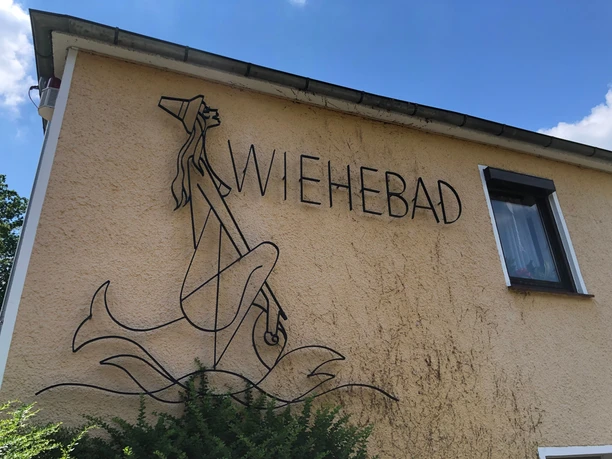 Wiehebad Metallkunstwerk eines stilisierten Fischermädchens mit langen Haaren und Hut an der Fassade des Wiehebads.