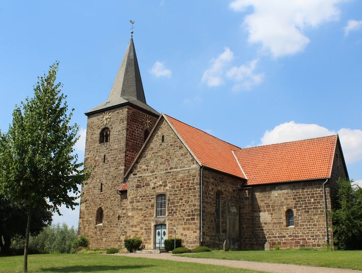 Kirche Windheim Eine historische Kirche aus Sandstein mit rotem Ziegeldach und markantem Glockenturm vor blauem Himmel.