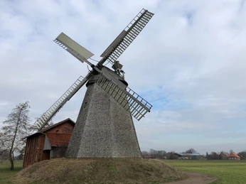 Windmühle Bierde Eine historische Windmühle in Bierde erhebt sich vor bewölktem Himmel, umgeben von einem weiten Feld.