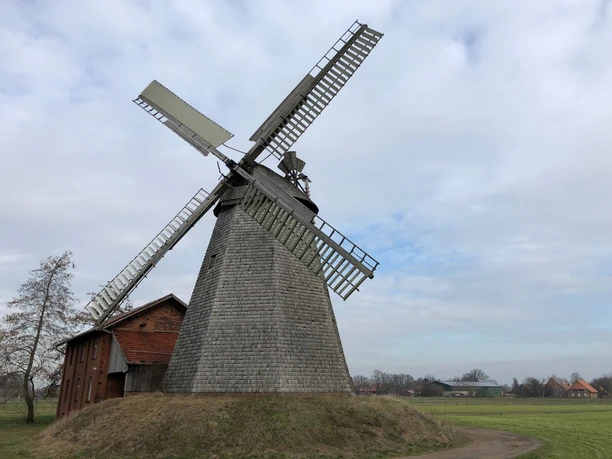 Windmühle Bierde Eine historische Windmühle in Bierde erhebt sich vor bewölktem Himmel, umgeben von einem weiten Feld.