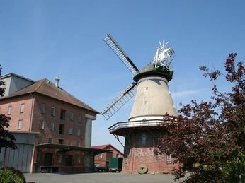 Historische Windmühle in Dörverden, umgeben von Backsteingebäuden, unter strahlend blauem Himmel.