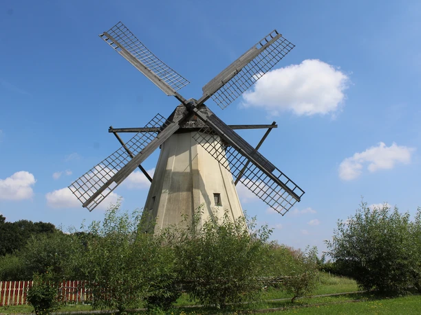 Windmühle Großenheerse Windmühle mit vier Schaufeln vor blauem Himmel und vereinzelten Wolken; umgeben von grüner Natur.