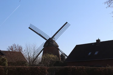 Windmühle mit markanten Flügeln und Backsteinbauten im Vordergrund unter blauem Himmel in Nienburg.