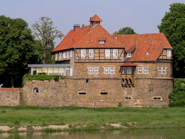 Schloss Petershagen Historisches Schloss Petershagen mit markanten Fachwerkelementen und rotem Ziegeldach am Weserufer.