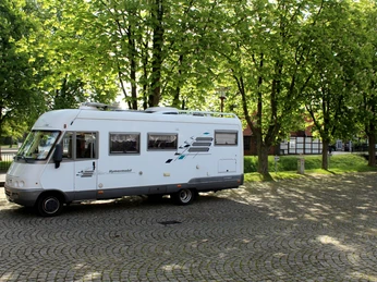 Ein Wohnmobil steht auf einem gepflasterten Stellplatz in Uchte, umgeben von grünen Bäumen.