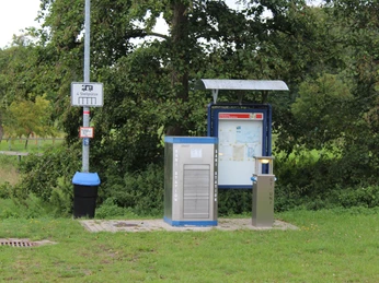 Entsorgungsstation Wohnmobilstellplatz Steyerberg Entsorgungsstation mit Abfallsammler und Infotafel auf einem Grasplatz, umgeben von grünen Bäumen.