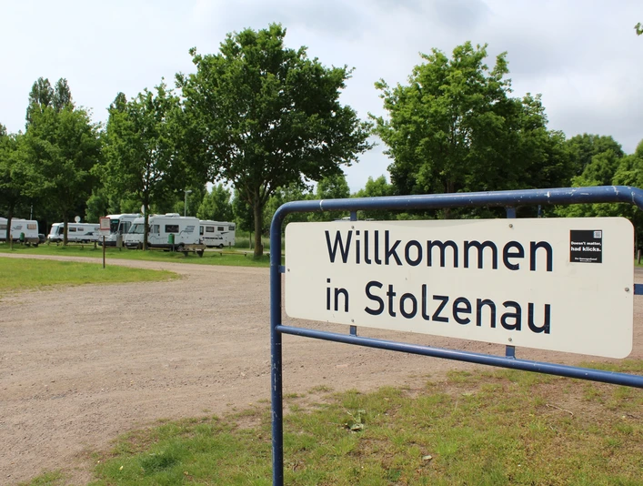 Willkommen in Stolzenau: Wohnmobilstellplatz, umgeben von grünen Bäumen und zahlreichen Wohnmobilen.
