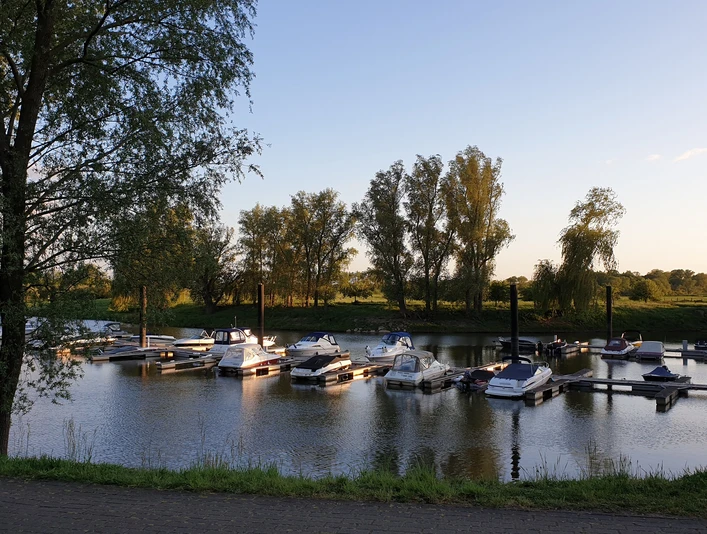 Uesener Bootshafen Eine ruhige Wasserstelle mit vertäuten Booten, umgeben von Bäumen unter einem klaren Abendhimmel.