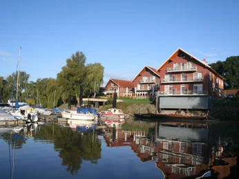 Hotel-Restaurant Bootshaus Hotel-Restaurant am Wasser mit Bootssteg und mehreren anlegenden Booten, umgeben von grünen Bäumen.