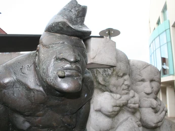 Skulptur eines Zigarrenmachers mit markantem Gesicht, flankiert von zwei neugierig beobachtenden Figuren.