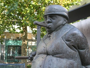 Skulptur eines Zigarrenmachers aus Metall, mit dickem Bauch und Zigarren in beiden Händen.