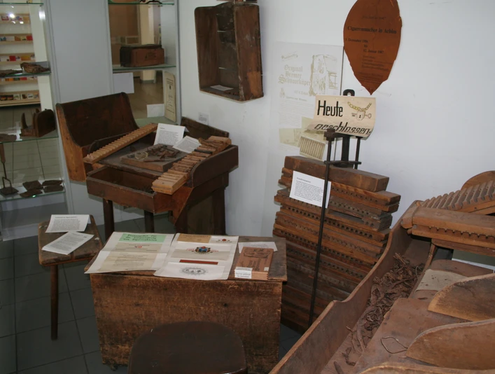 Ein kleiner Raum mit historischen Werkzeugen und Materialien zur Zigarrenherstellung in einer Ausstellung.