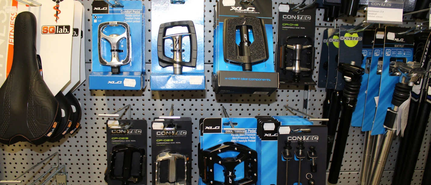 Fahrradzubehör Eine Auswahl an Fahrradzubehör, darunter Pedale und Kupplungen, auf einer grauen Lochwand montiert.