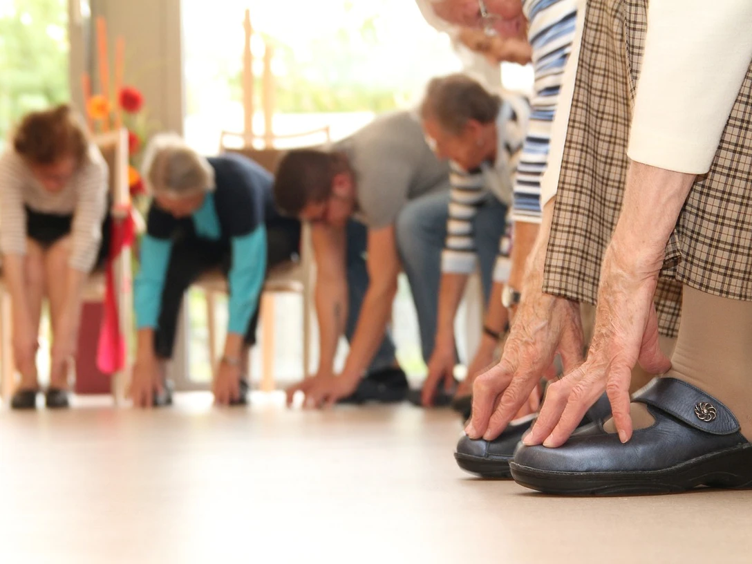 Seniorengymnastik Ältere Menschen führen gemeinsam in einem hellen Raum Dehnübungen durch, unterstützen ihre Beweglichkeit.