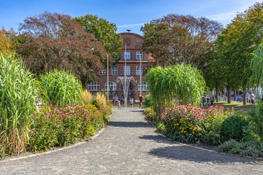 Rathauspark am Rathaus Büsum Ein rotes Backsteingebäude mit Springbrunnen und Pflanzen.