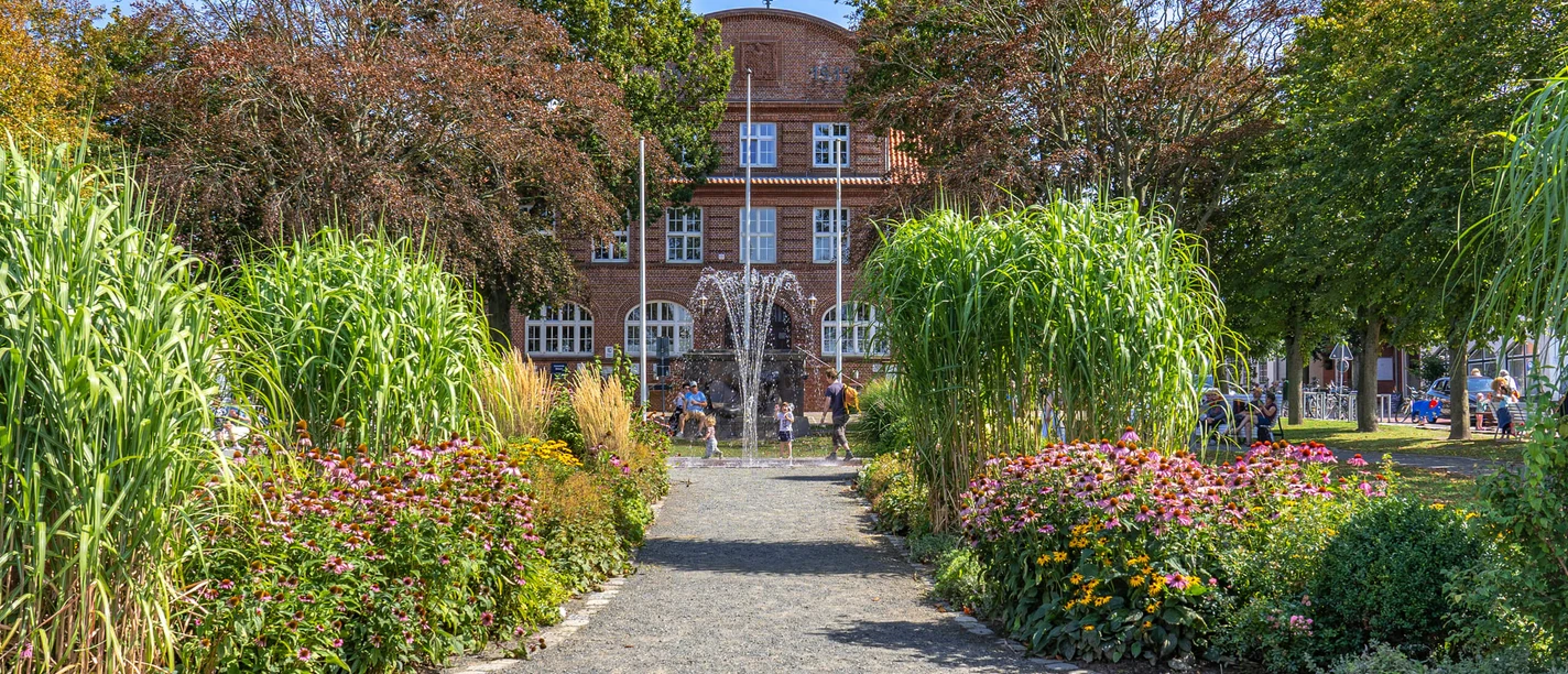 Rathauspark am Rathaus Büsum Ein rotes Backsteingebäude mit Springbrunnen und Pflanzen.
