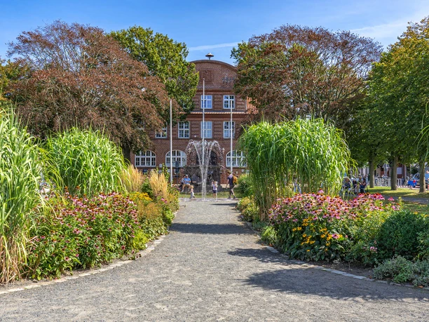 Rathauspark am Rathaus Büsum Ein rotes Backsteingebäude mit Springbrunnen und Pflanzen.