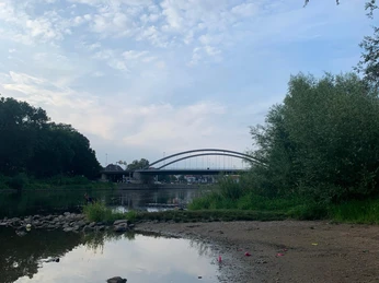 Ruhiger Sandstrand an der Weser, im Hintergrund eine elegante Bogenbrücke und grünes Ufer.