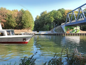 Schiffsanleger am Schloss Benkhausen Schiffsanleger am Schloss Benkhausen mit Brücke und umgebendem Wald, ruhige Wasseroberfläche.