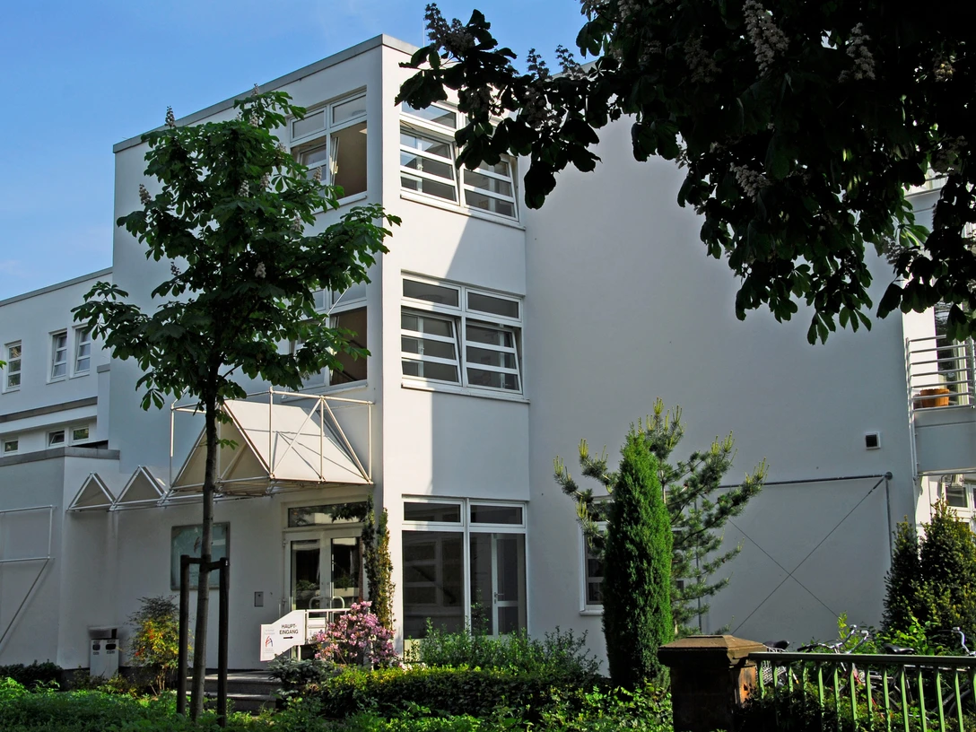 Artemed Fachklinik Prof. Dr. Dr. Salfeld Auf dem Bild ist die weiße Fassade der Klinik zu sehen, die ein modernes Gebäude darstellt. Umgeben wird es von Bäumen, die eine natürliche Atmosphäre schaffen.