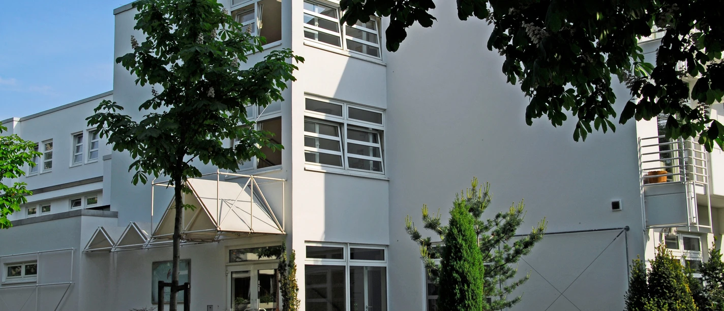 Artemed Fachklinik Prof. Dr. Dr. Salfeld Auf dem Bild ist die weiße Fassade der Klinik zu sehen, die ein modernes Gebäude darstellt. Umgeben wird es von Bäumen, die eine natürliche Atmosphäre schaffen.