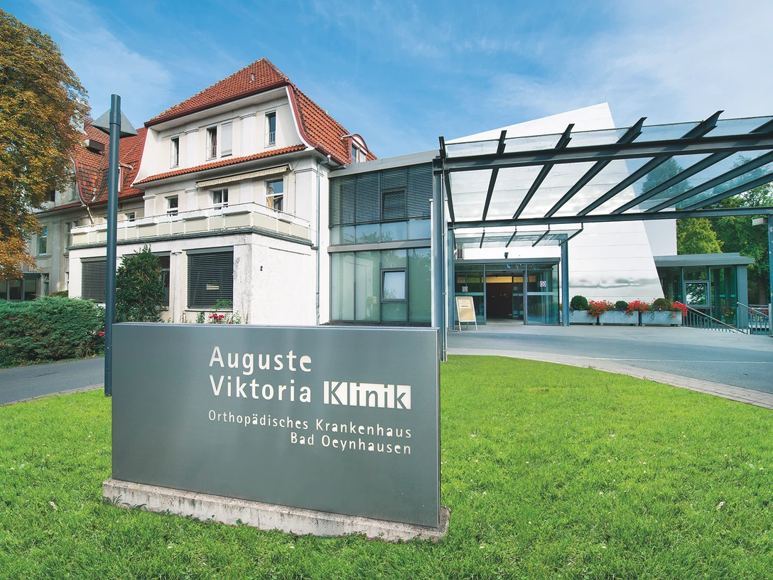 Auguste-Viktoria-Klinik Das Bild zeigt die Auguste-Viktoria-Klinik mit einem modernen Eingangsbereich und einem historischen Gebäude im Hintergrund. Im Vordergrund steht ein Schild mit dem Namen der Klinik, während eine Überdachung den Eingangsbereich überspannt.