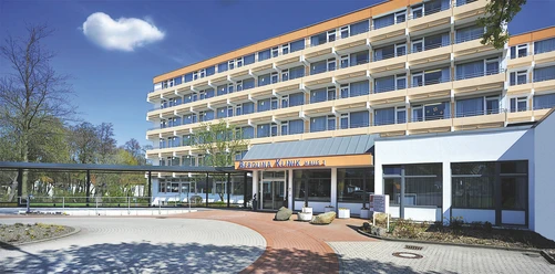 Berolina Klinik Das Bild zeigt die Außenansicht der Berolina Klinik in Bad Oeynhausen. Viele Balkone sind sichtbar, mit großen Fenstern, die einzelne Zimmer der Patienten zeigen. Der Eingangsbereich wirkt offen, und ein großer Hof ist ebenfalls zu sehen.
