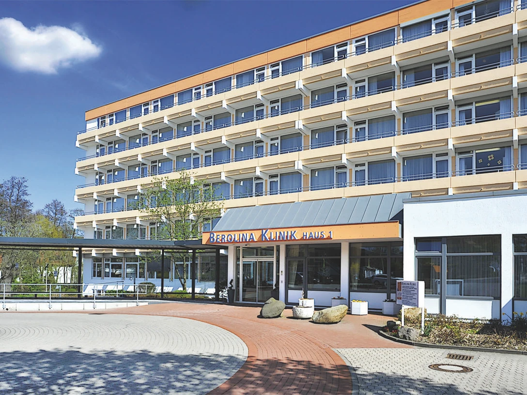 Berolina Klinik Das Bild zeigt die Außenansicht der Berolina Klinik in Bad Oeynhausen. Viele Balkone sind sichtbar, mit großen Fenstern, die einzelne Zimmer der Patienten zeigen. Der Eingangsbereich wirkt offen, und ein großer Hof ist ebenfalls zu sehen.