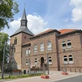 Kirchplatz mit historischer Kirche und Kriegerdenkmal, umgeben von Bäumen unter blauem Himmel.