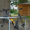 Rad-Rastplatz Retzen Fahrrad steht an Metallständer vor Holzhäuschen, umgeben von Bäumen und einem Picknicktisch.