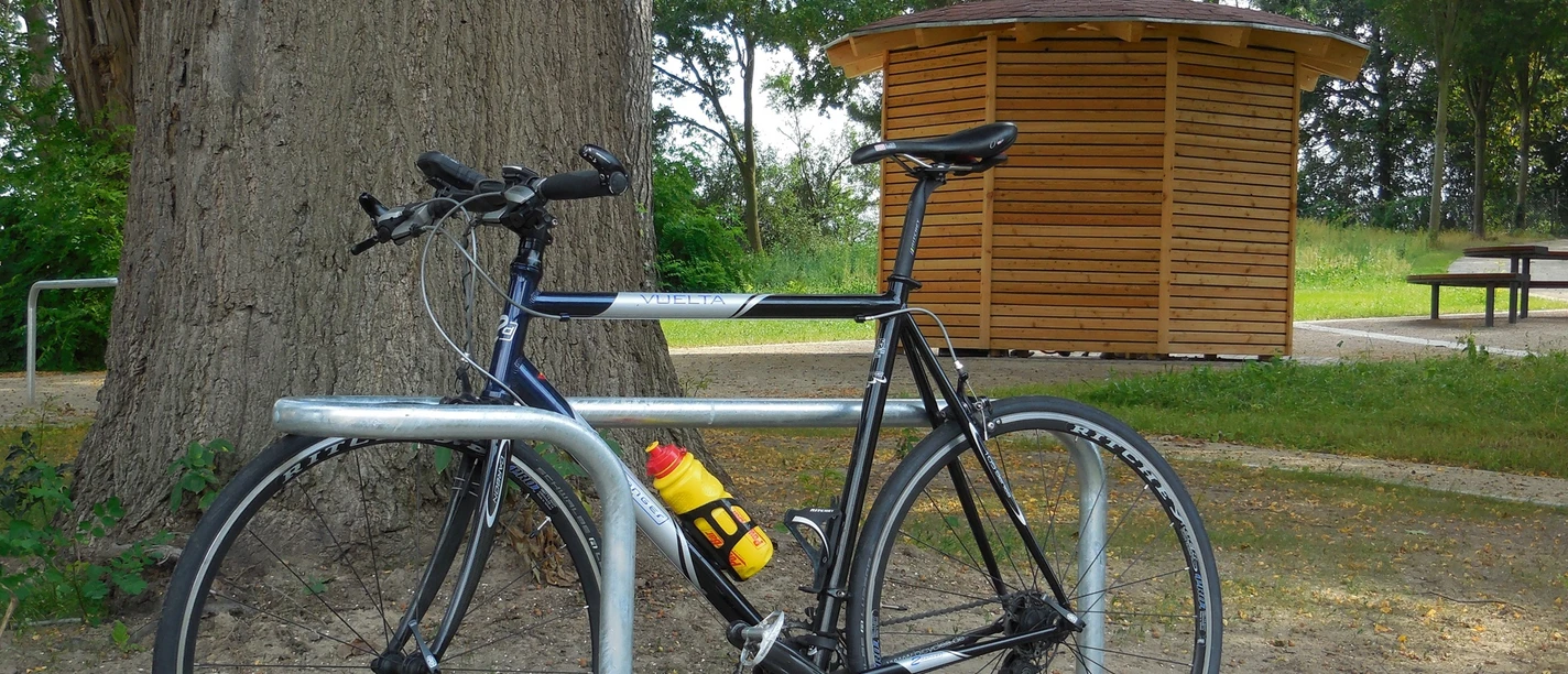 Rad-Rastplatz Retzen Fahrrad steht an Metallständer vor Holzhäuschen, umgeben von Bäumen und einem Picknicktisch.