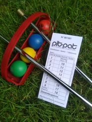 PitPat Hümmlinger Land Bunte PitPat-Bälle und Schläger liegen auf Gras neben einer Spielkarte mit Punkten und Spielfeldnummern.